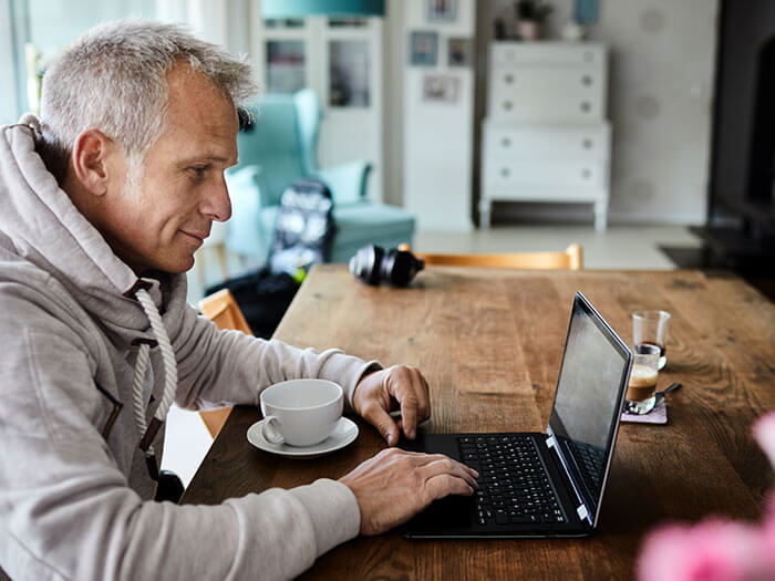 A man working on his computer and drinking coffee in his kitchen.