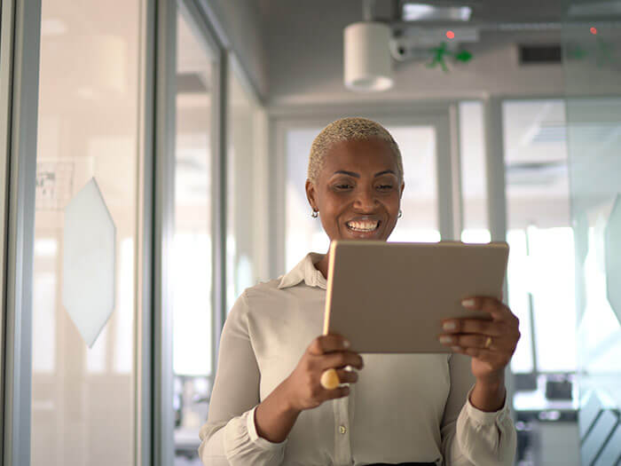 Femme d'affaires marchant tout en prenant un appel vidéo sur une tablette électronique dans un couloir de bureau.