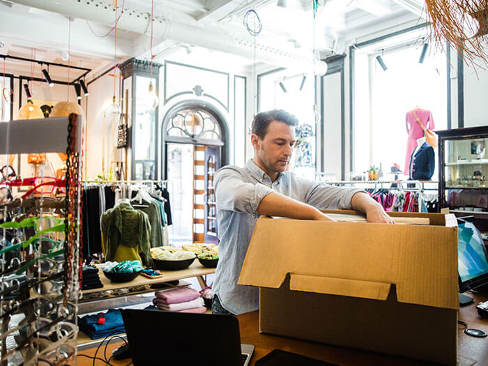 Propriétaire d'entreprise déballant une boîte en carton tout en travaillant dans un magasin de vêtements.