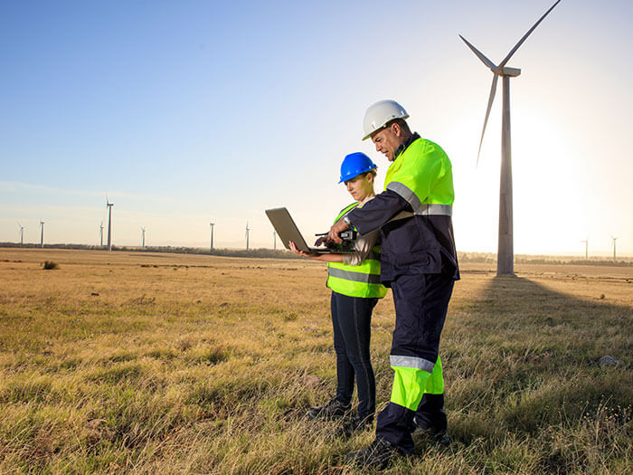 Deux ingénieurs avec un ordinateur portable discutent au milieu d'un parc éolien