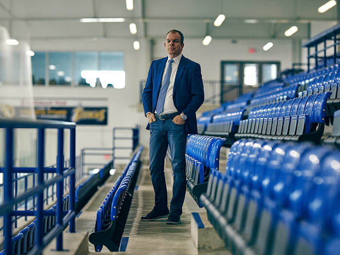 Portrait of Joe Resnick standing in the middle of a row of seats at a sports arena