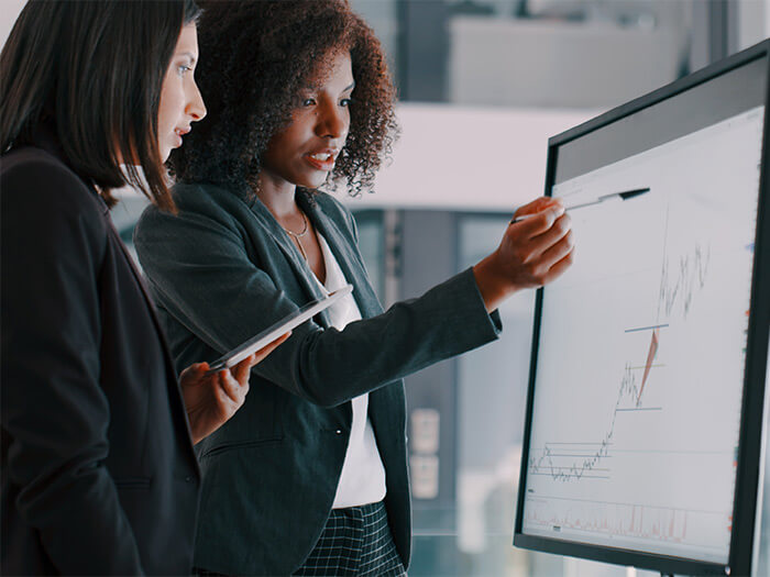 Deux jeunes femmes d'affaires utilisant un tableau blanc interactif pour analyser des données dans un bureau moderne