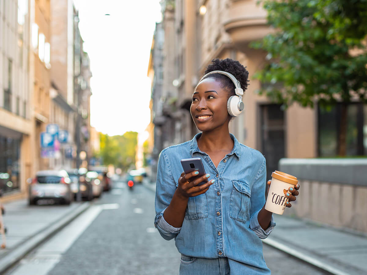 Woman with smart phone and reusable coffee cup walking in the city