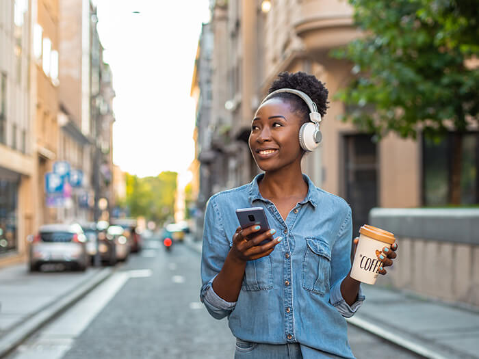 Femme avec un smartphone et une tasse à café réutilisable marchant dans la ville.