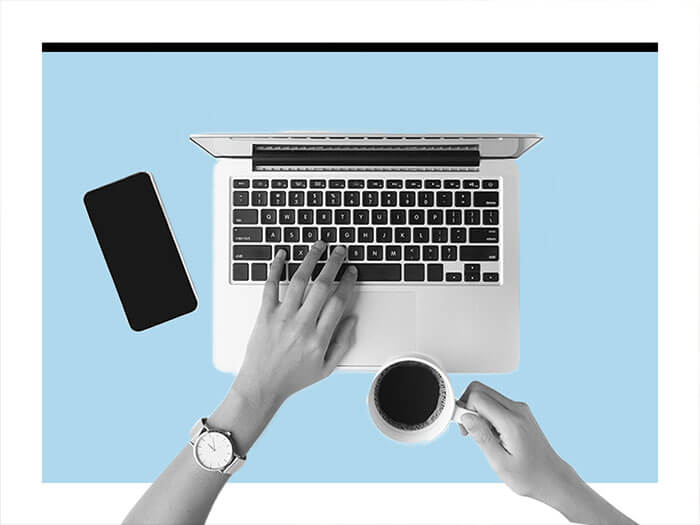 Overhead head shot of left hand working on lap top and right hand holding a cup of coffee
