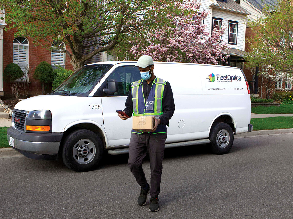A FleetOptics drivers is shown in front of a white van with a box in his hands