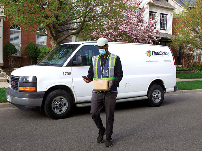 Un chauffeur de FleetOptics est montré devant une camionnette blanche avec une boîte dans les mains.
