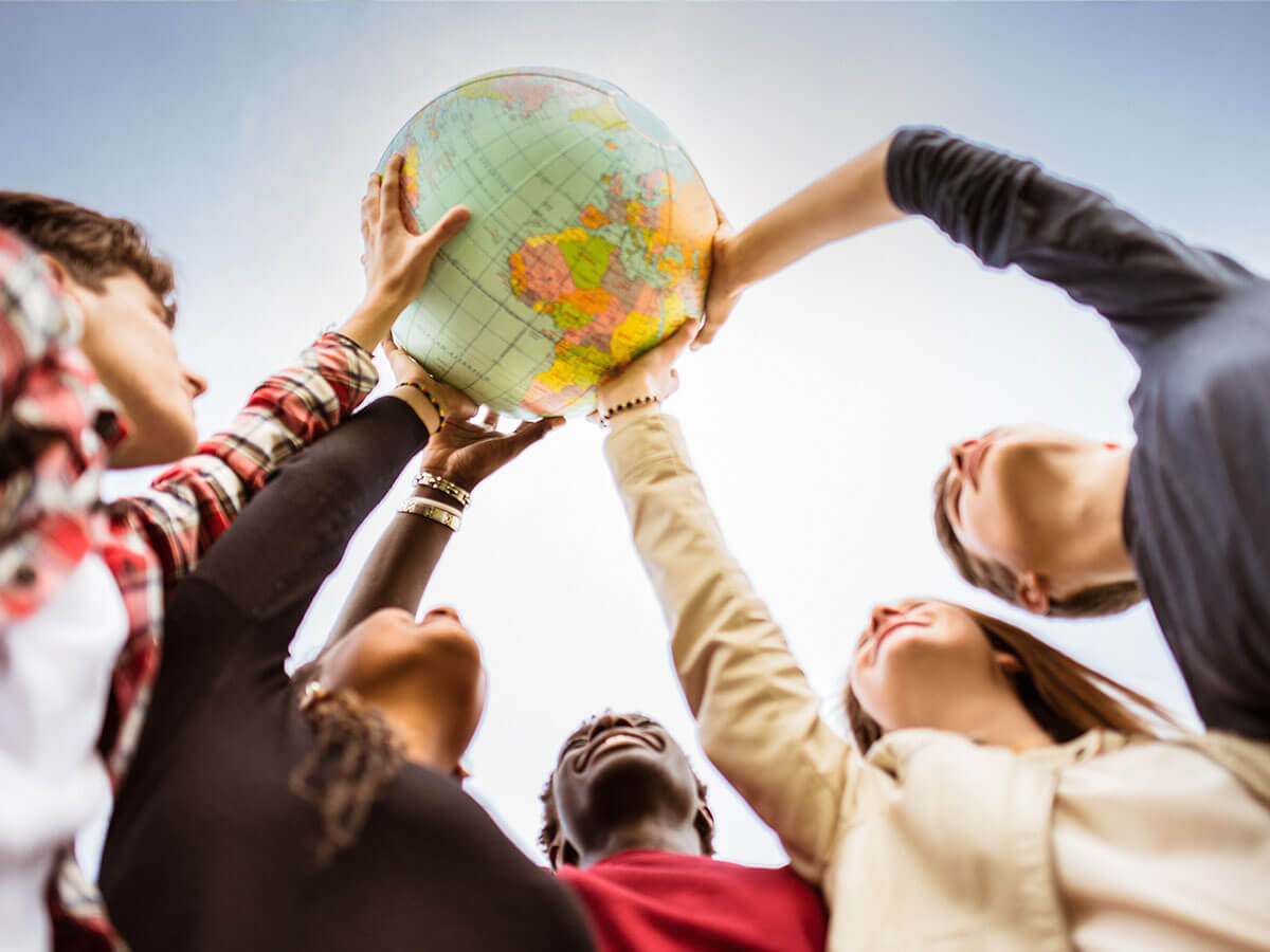 Cinq jeunes gens sont montrés à l'extérieur, tenant ensemble un globe terrestre