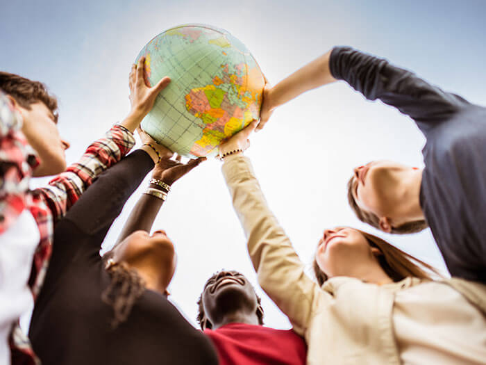 Cinq jeunes gens sont montrés à l'extérieur, tenant ensemble un globe terrestre