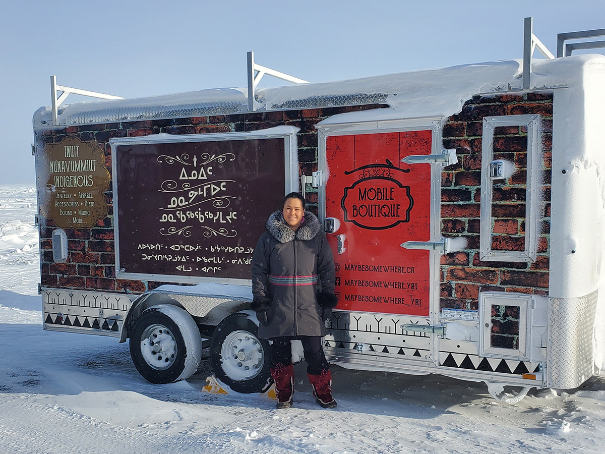 A woman stands in front of a trailer being used as a mobile store, with a snowy background