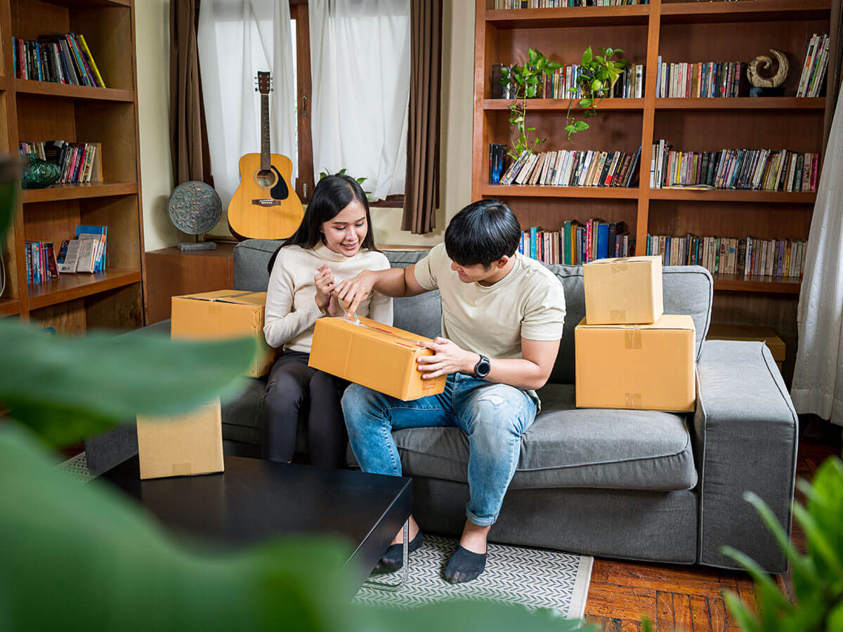 Two people sit on a couch while they open packages