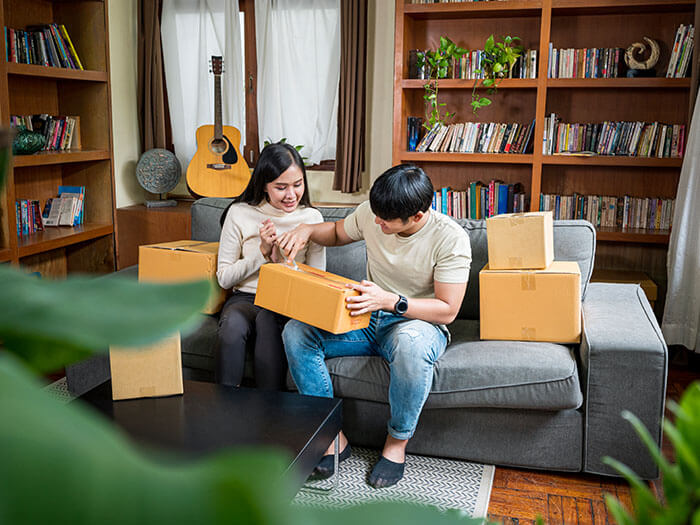 Two people sit on a couch while they open packages