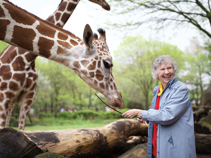 An older woman stands next to a giraffe