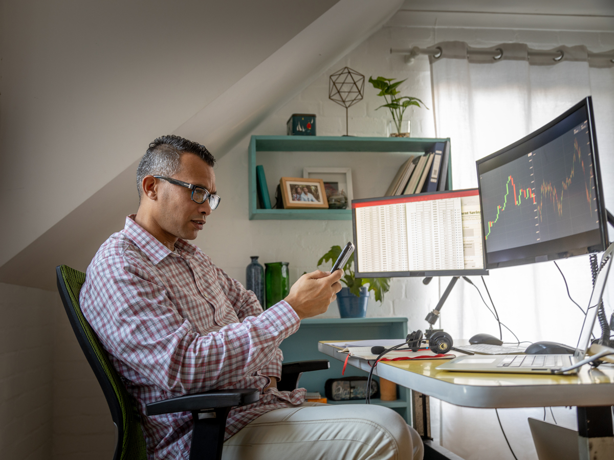 Homme assis à son bureau à domicile, consultant une application boursière sur son téléphone intelligent