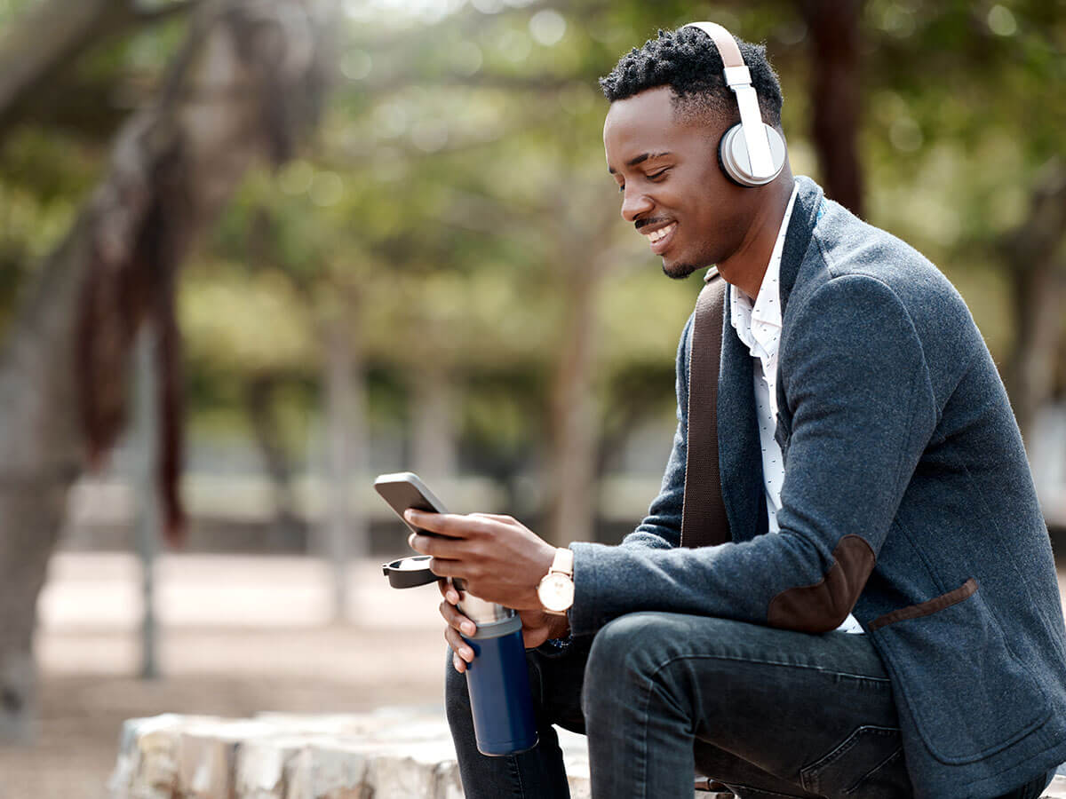 A man wears headphones while sitting outside looking at his phone 