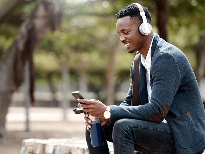 Un homme porte des écouteurs alors qu'il est assis dehors et regarde son téléphone. 