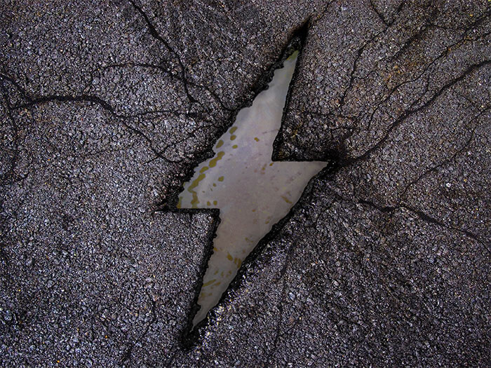 A closeup of a cracked pothole is shown on a road