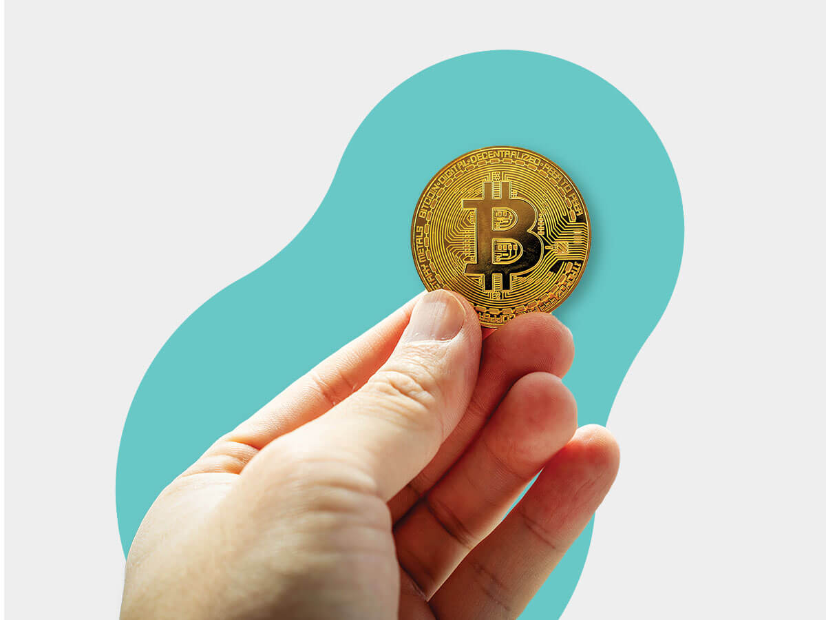 A hand holds a gold coin with the Bitcoin logo on it
