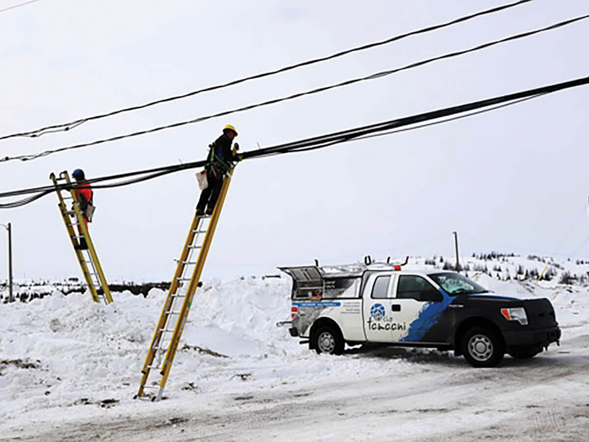 Des ouvriers réparent des câbles à fibres optiques dans une zone rurale enneigée. 