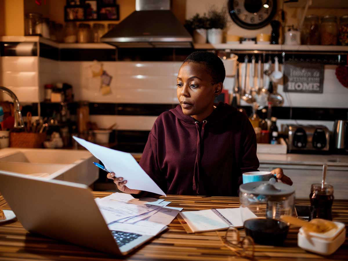 A woman sits at her kitchen counter with a laptop and papers
