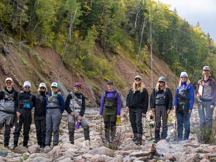 A group of women stand in front of a river with fly fishing rods