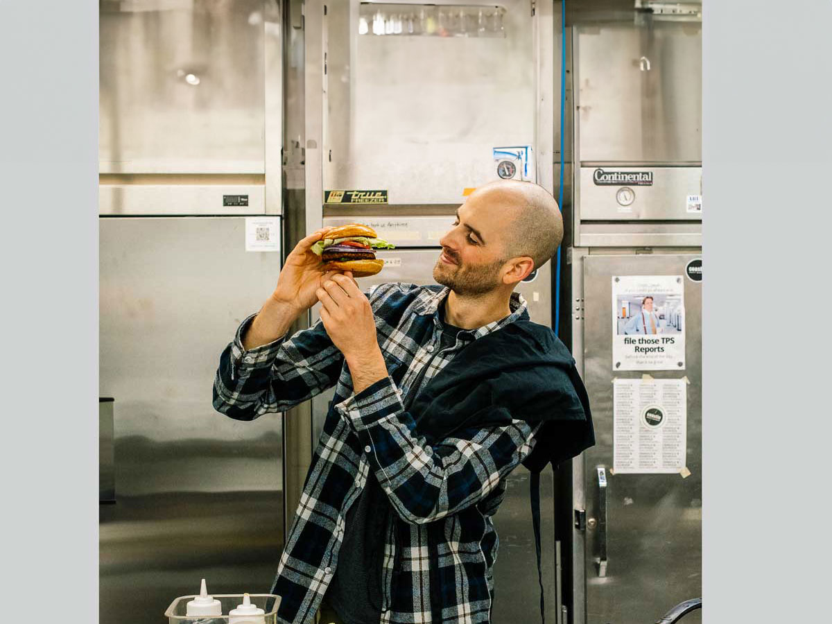 Alexander Cant tient un végéburger debout dans une cuisine industrielle