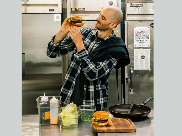 Ali Cant holds a burger up and looks at it in a kitchen 