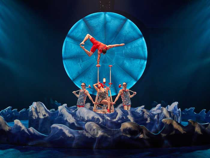 Four performers balance on top of each other in colourful costumes