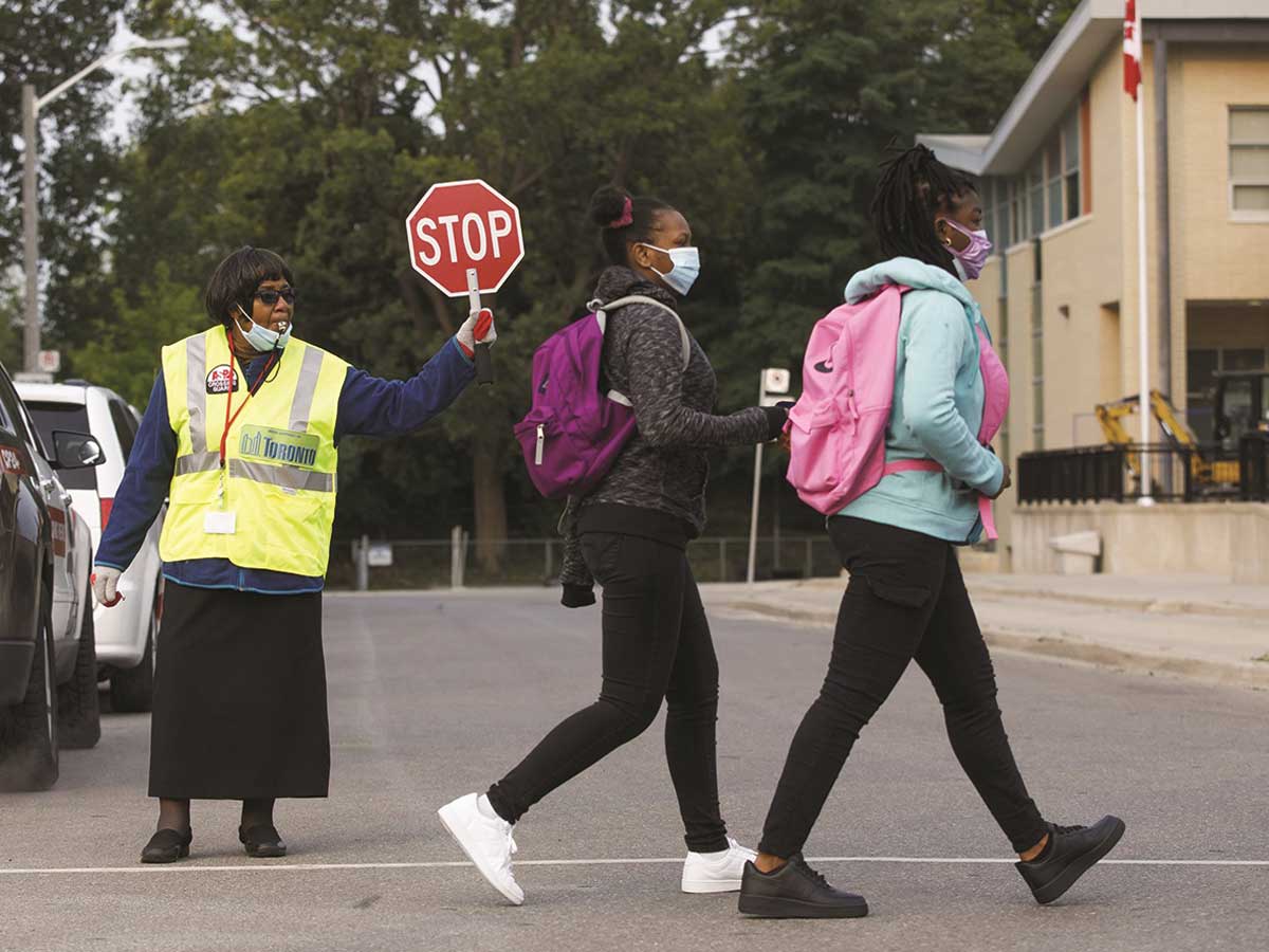 A crossing guard helps two students across the street
