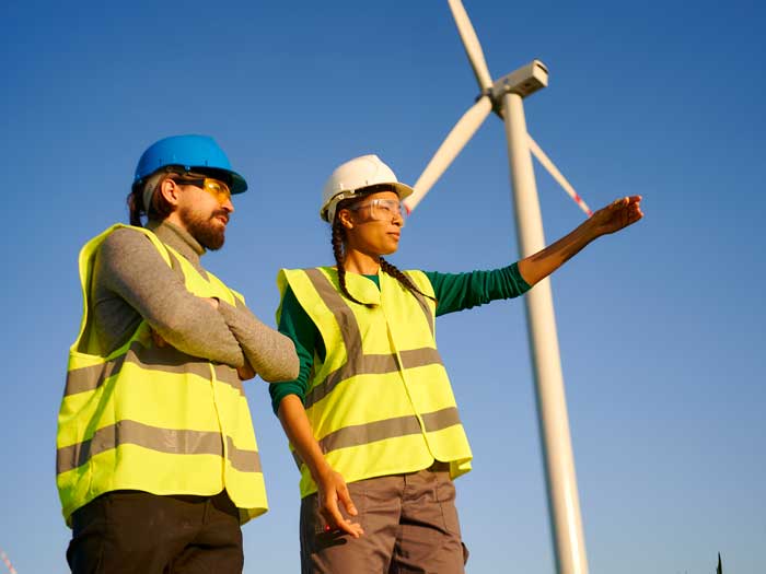 Two workers stand below a wind turbine