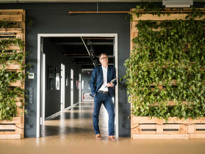 A businessman stands in an office next to a wall with plants on it