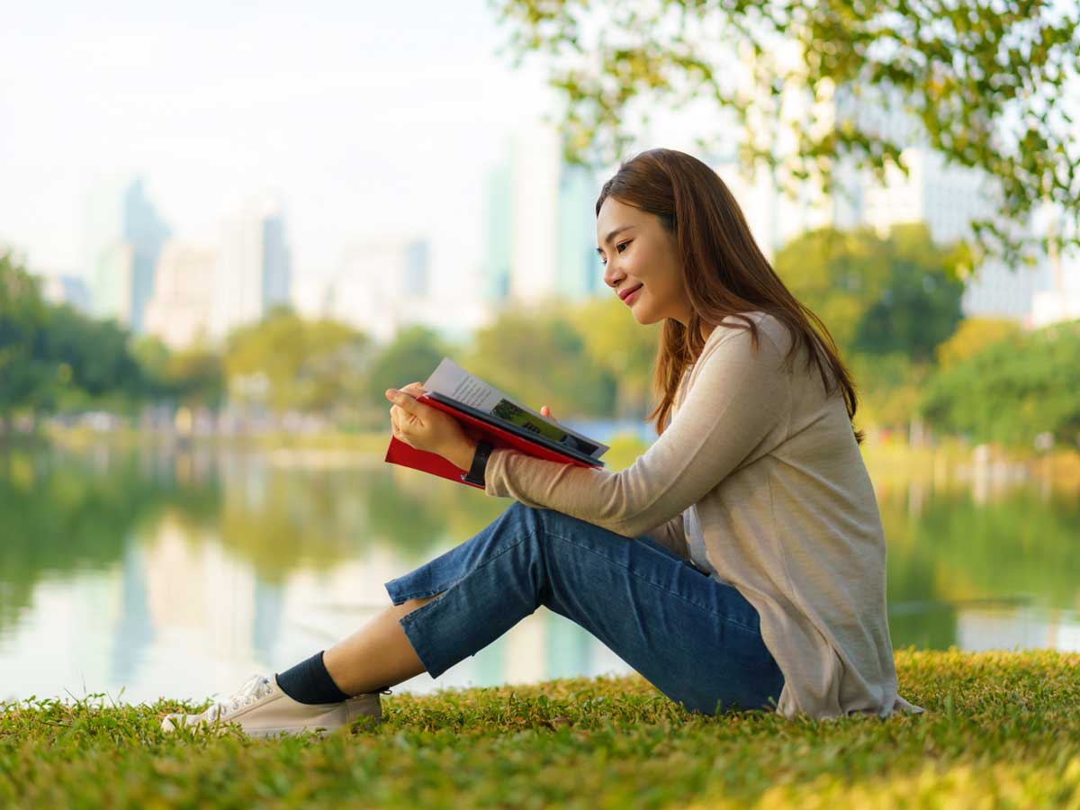 Une femme lit un livre au bord d’un étang.