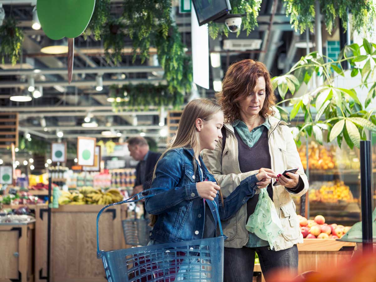 An adult and child look at a smartphone in a grocery store