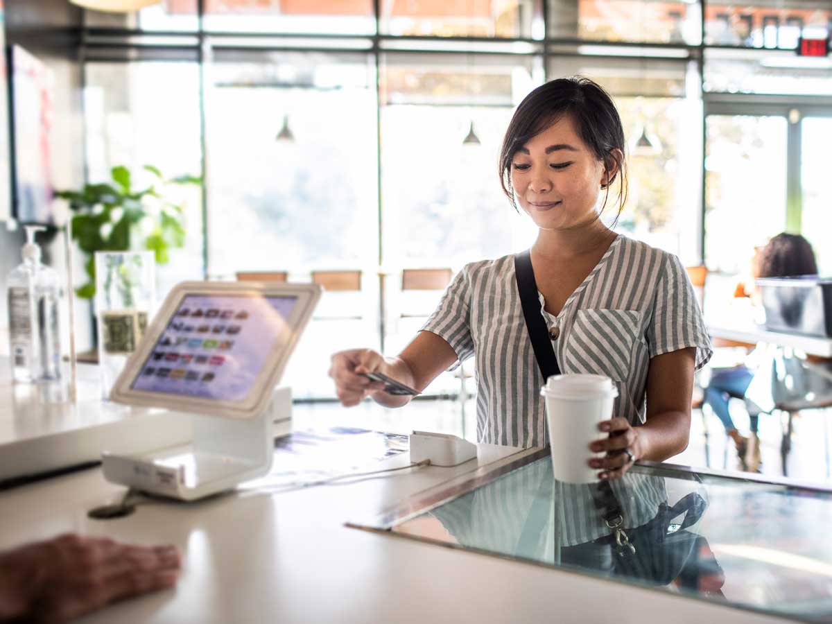 Une jeune femme utilise un lecteur de carte de crédit au comptoir d’un café 
