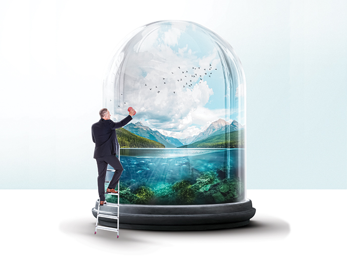 A man cleans a giant bell jar that shows a mountain view. 