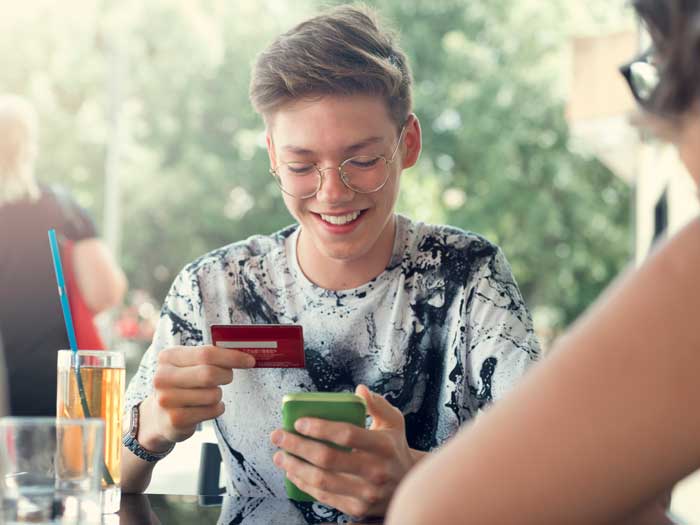 A young person holds a credit card and a phone at a cafe