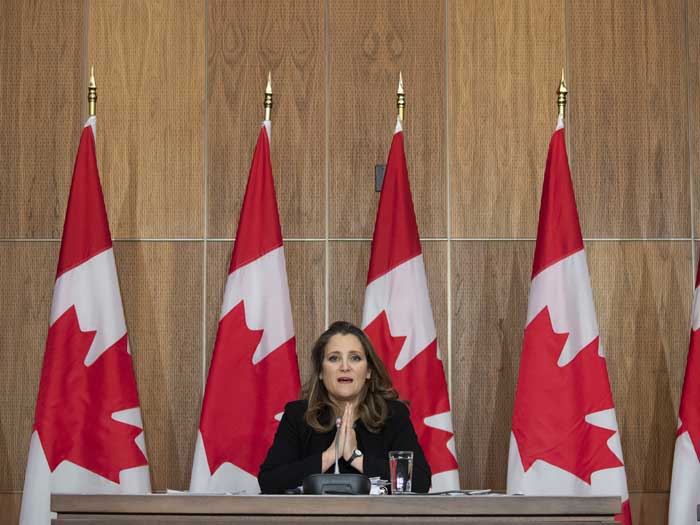 Chrystia Freeland is shown sitting in front of Canadian flags