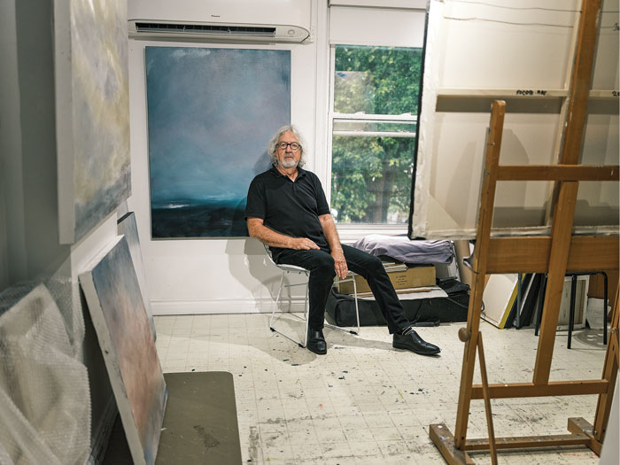 Artist Jacques Descoteaux sits in his studio surrounded by painted canvases of his art
