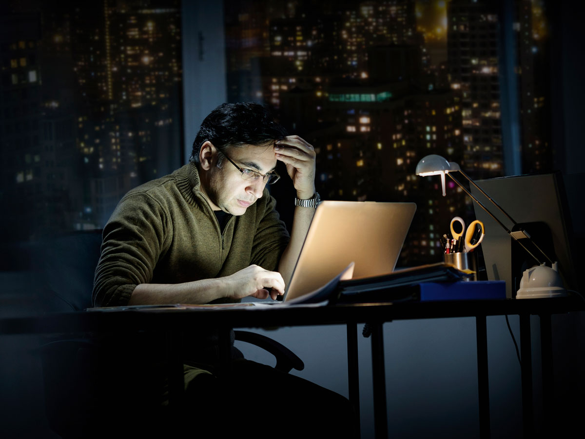 Un homme regarde un ordinateur portable dans son bureau, la nuit.