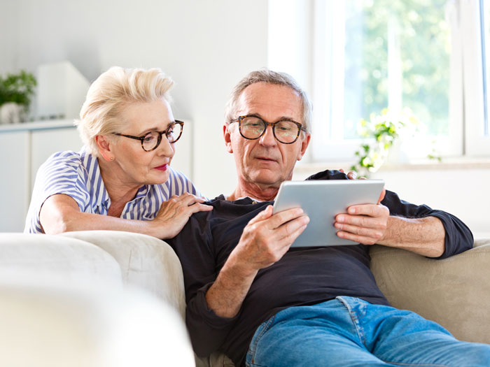 Un couple de personnes âgées consulte une tablette dans son salon.