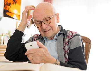 Old man sitting at table using cell phone 