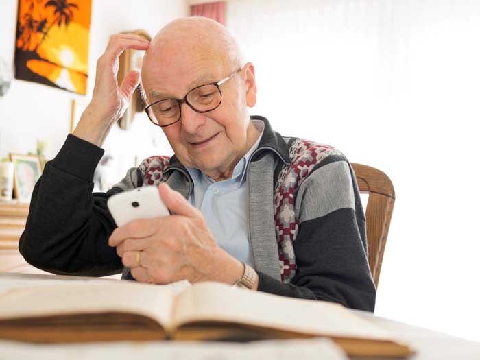 Old man sitting at table using cell phone 