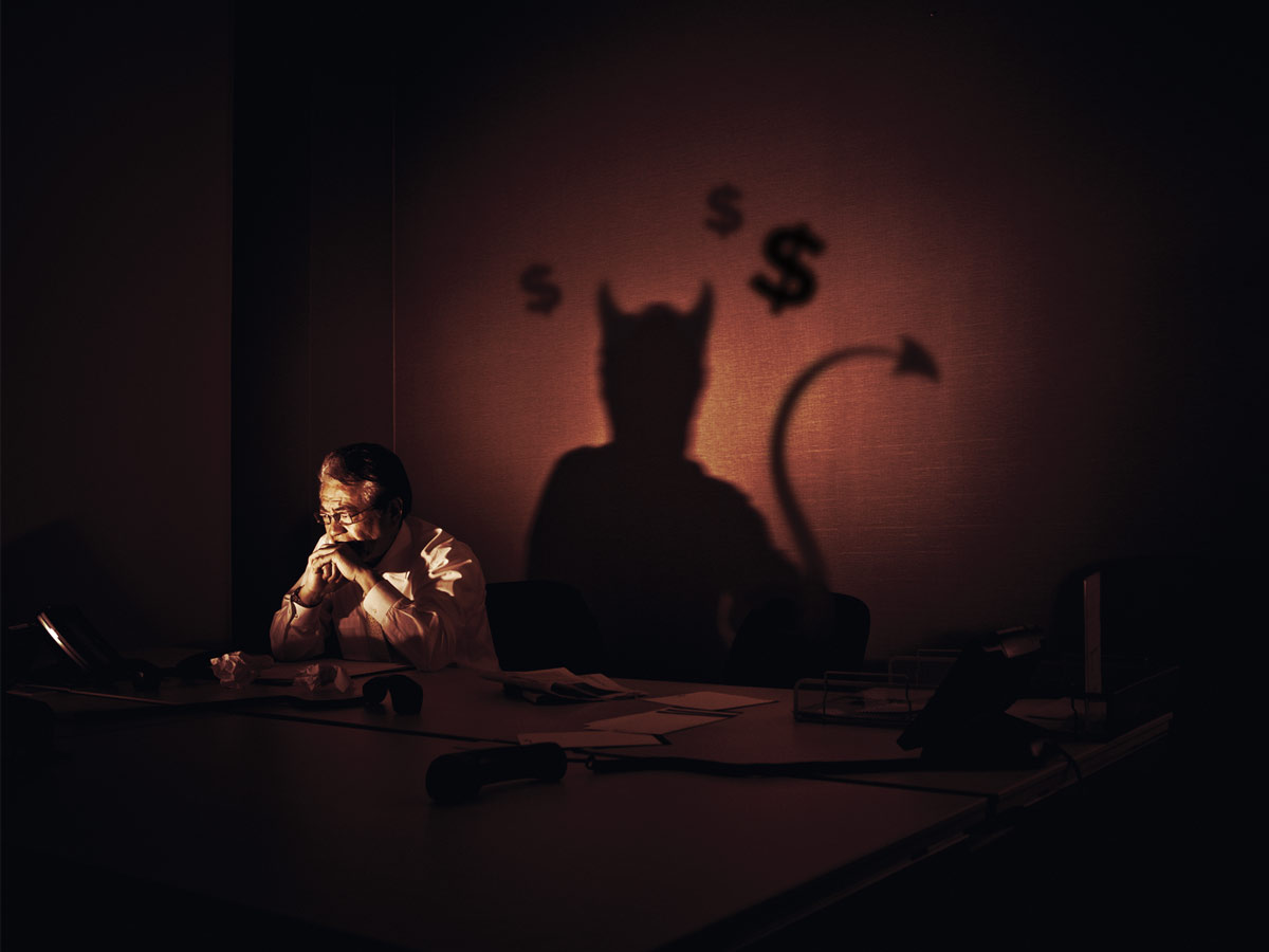 Man at desk casting a shadow of a devil 