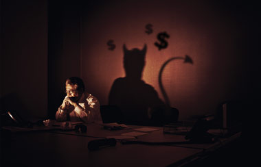 Man at desk casting a shadow of a devil 