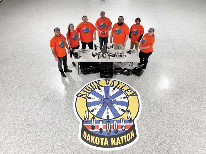 Group of people in orange shirts in front of large crest with the name Sioux Valley Dakota Nation
