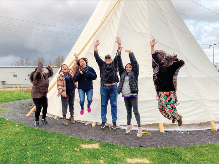 Group jumping in the air in front of a teepee