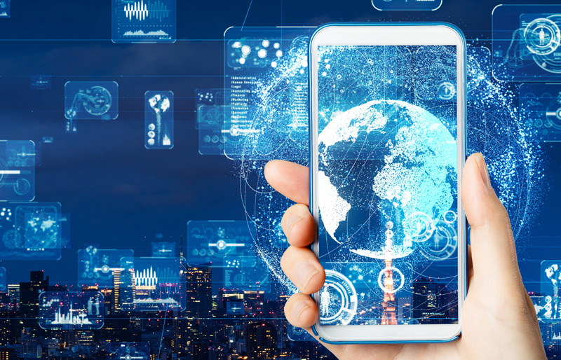 Cadrage sur la main d’une personne tenant un cellulaire sur un fond de paysage urbain nocturne et superposé à l’image, des montages graphiques représentant la technologie