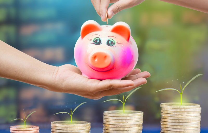 A close-up photograph of a parent holding a colourful piggy bank with a child depositing money. 