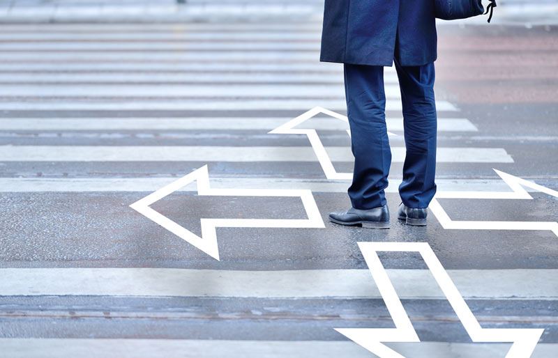 Man standing in crosswalk with four arrows pointing four different ways