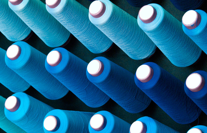 Trois rangées de bobines de fil de différentes nuances de bleu.